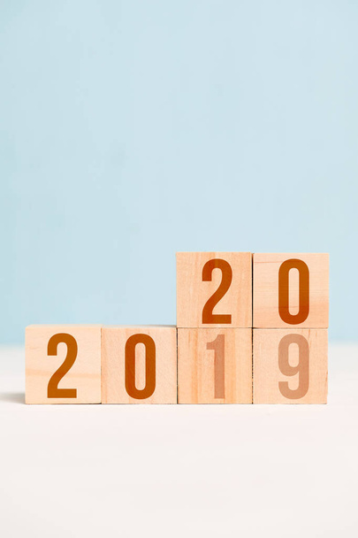 Numbers 2020 and 2019 on wooden cubes on a blue background. The concept of the change of the year. Vertical. Copy space. - Photo, Image