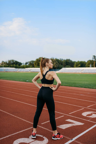 Vrouwelijke jogger staat op de startlijn, traint op het stadion. Vrouw doen stretching oefening voor het lopen op outdoor arena - Foto, afbeelding