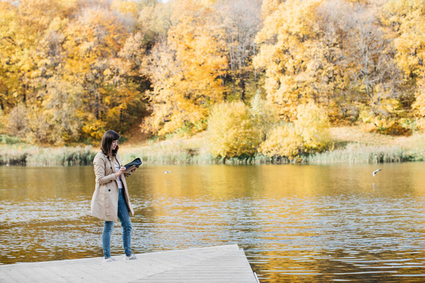Nuori tyttö luonnostelee järven lähellä syksyllä metsässä
. - Valokuva, kuva