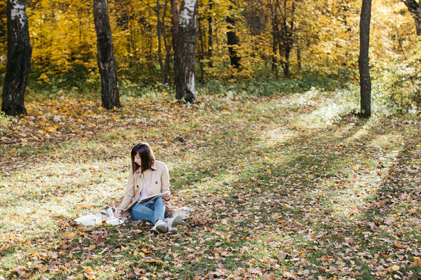 Ένα νεαρό κορίτσι ζωγραφίζει κοντά σε μια λίμνη το φθινόπωρο στο δάσος. Σκιτσάρω. Το κορίτσι έχει καλή διάθεση και είναι χαρούμενο. - Φωτογραφία, εικόνα