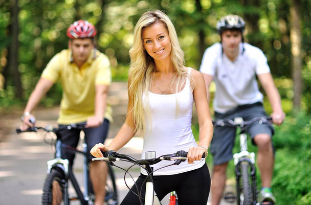 Portrait de jeune femme séduisante à vélo et deux hommes derrière elle
 - Photo, image