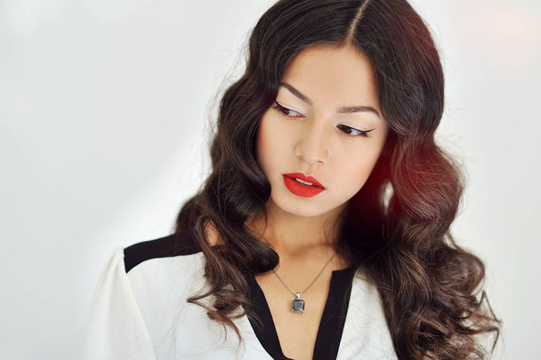 Mooi meisje met rode lippen en krullend zwart haar op witte achtergrond  - Foto, afbeelding