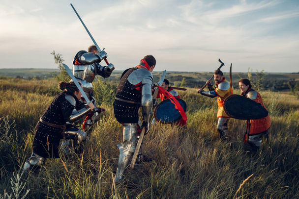 Keskiaikaiset ritarit panssarissa ja kypärissä taistelevat miekalla ja kirveellä. Panssaroitu muinainen soturi haarniskassa poseeraa kentällä.
 - Valokuva, kuva