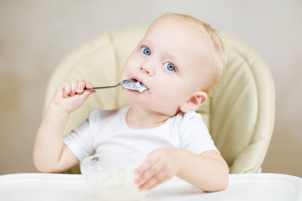 A little girl eats porridge with a spoon and thinks about something. - Foto, Imagem