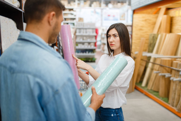 Jong stel kiezen wallpapers kleur in hardware winkel. Mannelijke en vrouwelijke klanten bekijken de goederen in de diy shop - Foto, afbeelding
