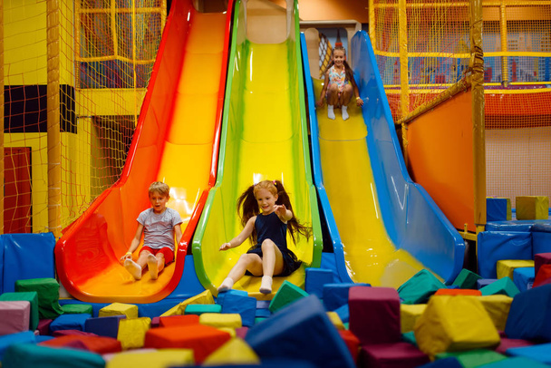 Μικρά παιδιά που διασκεδάζουν σε φουσκωτή τσουλήθρα, παιδική χαρά στο κέντρο διασκέδασης. Χώρος παιχνιδιού σε εσωτερικούς χώρους, playroom - Φωτογραφία, εικόνα