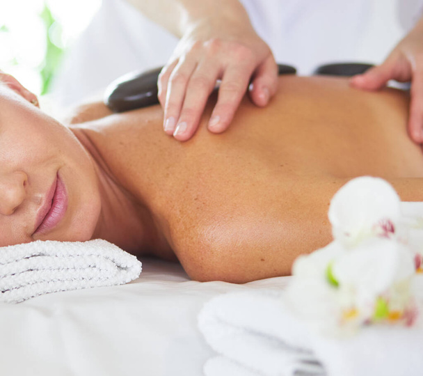 Beautiful young woman with eyes closed receiving hot stone massage at salon spa - Φωτογραφία, εικόνα