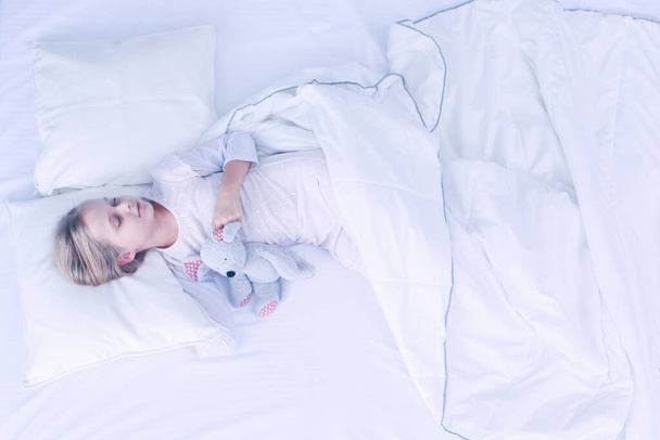 Child little girl sleeps in the bed with a toy teddy bear. - 写真・画像
