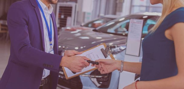 Car salesman sells a car to happy customer in car dealership and hands over the keys - Valokuva, kuva