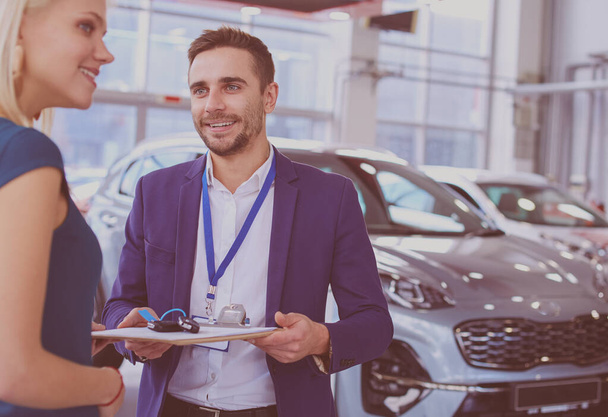 Car salesman sells a car to happy customer in car dealership and hands over the keys - Foto, imagen