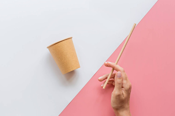 eco natural paper coffee cup, hand and straw flat lay on white and pink background. sustainable lifestyle concept. zero waste, plastic free items. stop plastic pollution. Top view, overhead, mockup - Φωτογραφία, εικόνα