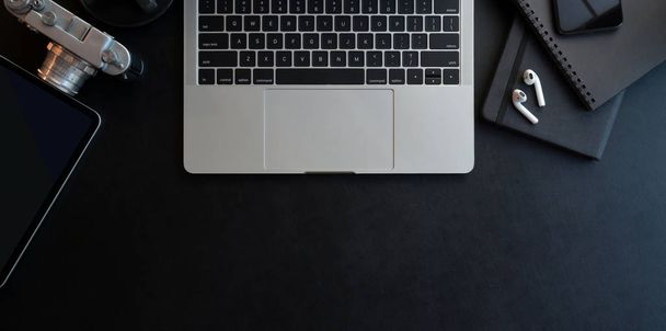 Vista dall'alto del luogo di lavoro scuro moderno con computer portatile aperto e forniture per ufficio su sfondo nero scrivania in pelle
   - Foto, immagini