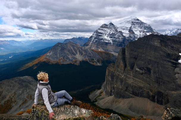 Succesvolle vrouwelijke wandelaar zittend op bergtop genietend van uitzicht op bergdal met gele lariksbomen van bovenaf. Lake Louise gebied. Nationaal park Banff. - Alberta. Zwitserland. - Foto, afbeelding