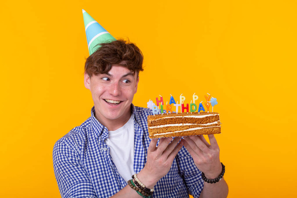 Positiivinen nuori mies, jolla on onnellinen syntymäpäivä kakku poseeraa keltaisella taustalla
. - Valokuva, kuva