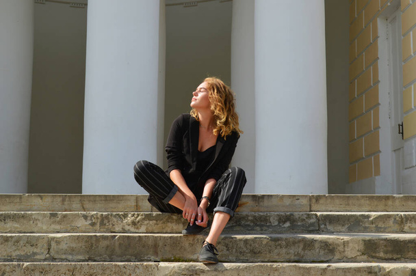 Uma jovem mulher sexy em um terno preto de negócios está sentada
 - Foto, Imagem