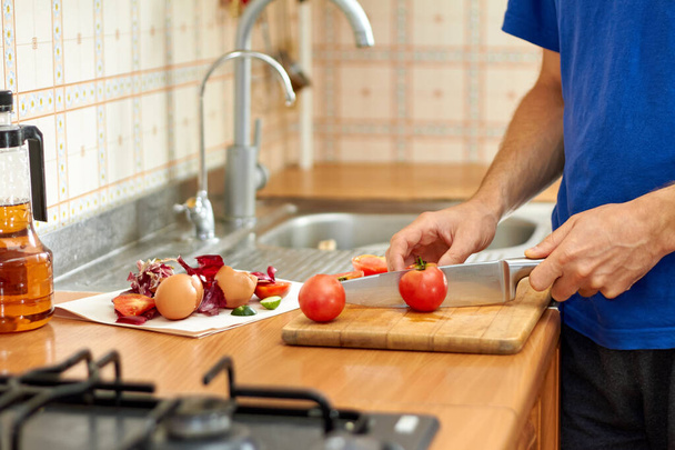 Muž krájí rajčata. Plýtvání jídlem a odpadky při přípravě jídla v kuchyni. Detailní záběr, selektivní zaměření - Fotografie, Obrázek