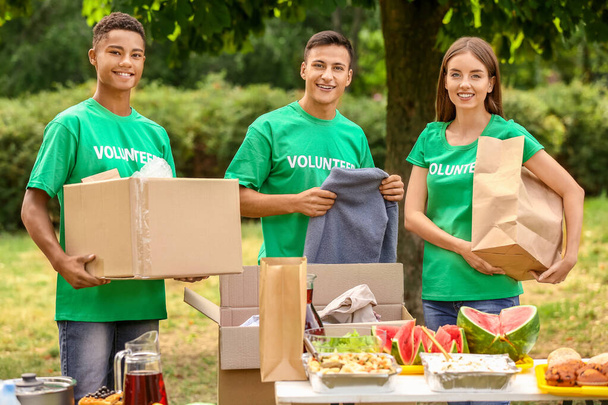 Jóvenes voluntarios con comida y ropa para los pobres al aire libre
 - Foto, Imagen