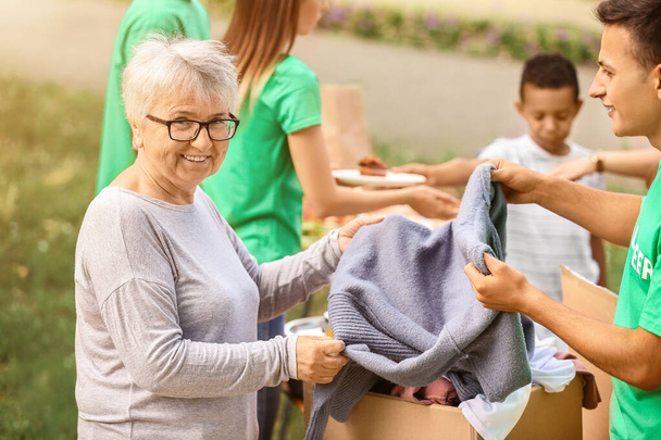 Jonge vrijwilliger geeft nieuwe kleren voor arme oudere vrouw buiten - Foto, afbeelding