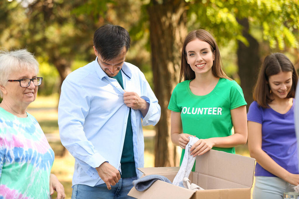 Jonge vrijwilliger geeft nieuwe kleren voor arme mensen buiten - Foto, afbeelding