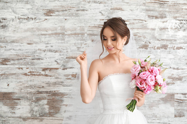 Portrait of beautiful young bride with wedding bouquet on wooden background - Photo, Image