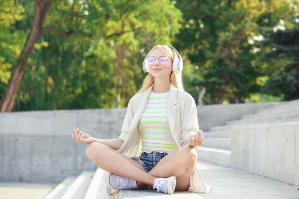 Mooie jonge vrouw luisteren naar muziek en mediteren buiten - Foto, afbeelding