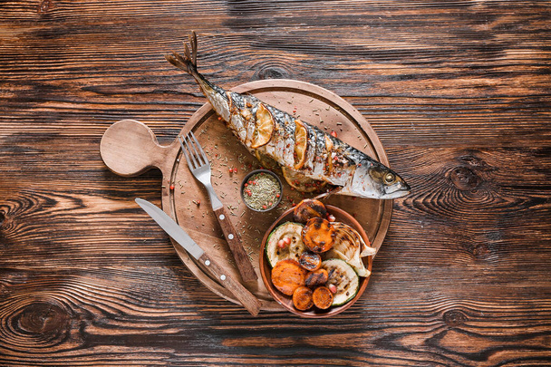 Board with prepared mackerel fish and vegetables on wooden background - Photo, Image