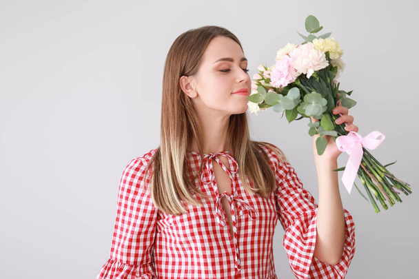 Beautiful young woman with bouquet of carnation flowers on light background - Photo, Image
