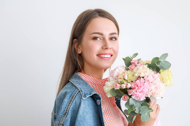 Beautiful young woman with bouquet of carnation flowers on light background - Fotó, kép