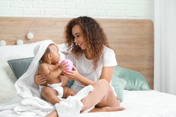 Νεαρή Αφρο-Αμερικανίδα μητέρα με χαριτωμένο μωρό κάθεται στο κρεβάτι μετά το μπάνιο - Φωτογραφία, εικόνα