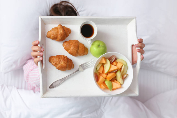 Jeune femme tenant plateau avec petit déjeuner savoureux tout en étant couché au lit
 - Photo, image