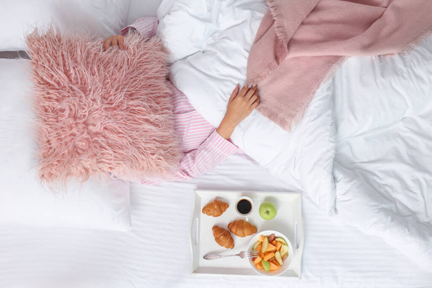 Tray with tasty breakfast near sleeping woman on bed - Photo, Image