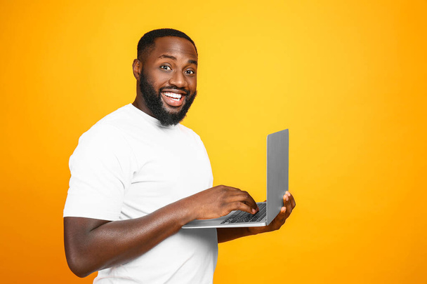 Όμορφος Αφρο-Αμερικανός άνδρας με laptop στο φόντο χρώμα - Φωτογραφία, εικόνα