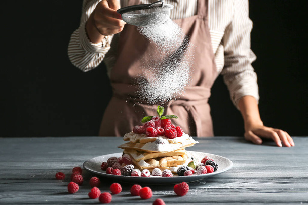 Kobieta posypuje cukrem w proszku belgijskie wafle na stole - Zdjęcie, obraz