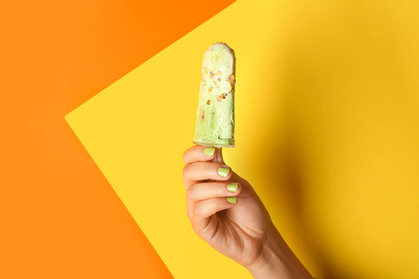 Female hand with tasty pistachio ice cream on color background - Foto, imagen