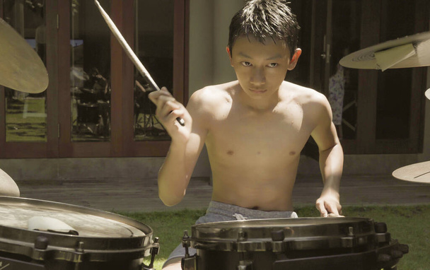 Asian American teenager playing drums. Summer portrait of handsome young boy practicing on drum kit at home garden rehearsing rock song enjoying his hobby - Foto, immagini