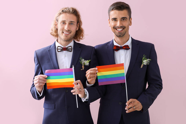 Happy gay couple with LGBT flags on their wedding day against color background - Fotó, kép