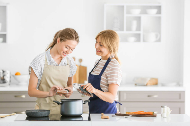 Young woman and her mother cooking together in kitchen - Foto, Imagen