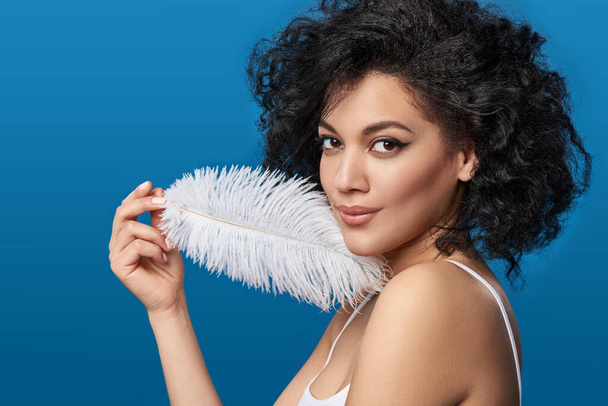Beautiful mixed race woman holding white ostrich feather - Φωτογραφία, εικόνα