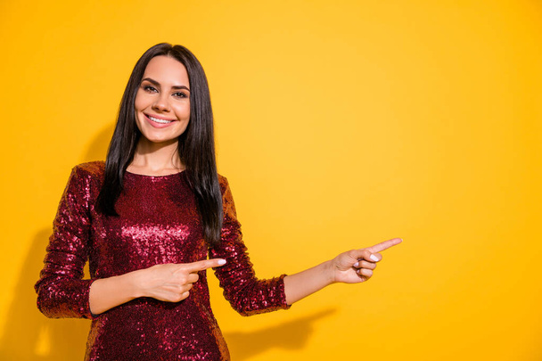 Photo of amazing lady indicating fingers to empty space on banner advising low shopping prices wear shine red dress isolated yellow color background - 写真・画像