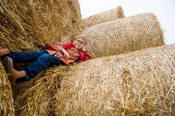 Happy school boy playing in haystack. Blond child in red jacket. Holiday in ecological farm. Education in agriculture. - Photo, image