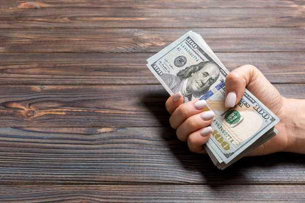 Perspective view of female hand giving one hundred dollar bills on wooden background. Charity and donation concept with copy space - Photo, Image