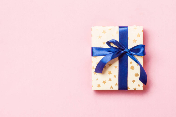 verpakt Kerstmis of andere met de hand gemaakte vakantie cadeau in papier met blauw lint op roze achtergrond. Aanwezig doos, decoratie van geschenk op gekleurde tafel, bovenaanzicht met kopieerruimte - Foto, afbeelding