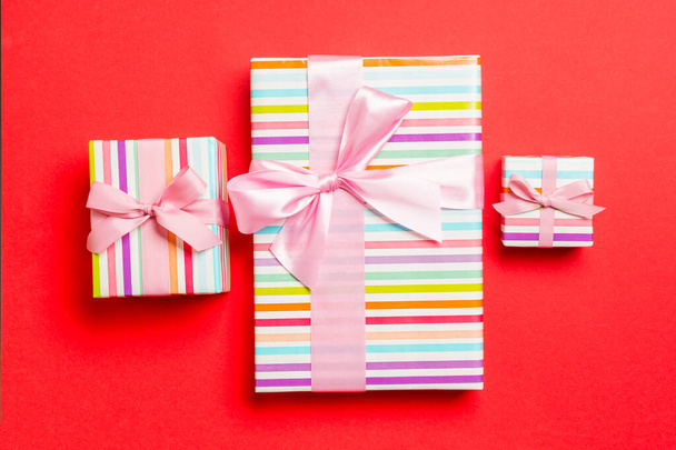 verpackte Weihnachten oder andere Feiertage handgemachtes Geschenk in Papier mit rosa Schleife auf rotem Hintergrund. Geschenkbox, Geschenkdekoration auf farbigem Tisch, Draufsicht - Foto, Bild