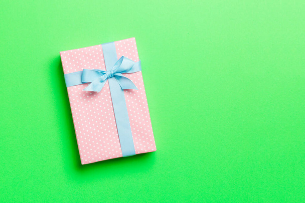 verpakt Kerstmis of andere met de hand gemaakte vakantie cadeau in papier met blauw lint op groene achtergrond. Aanwezig doos, decoratie van geschenk op gekleurde tafel, bovenaanzicht met kopieerruimte - Foto, afbeelding