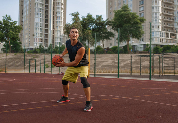 Basketbalista se připravuje na natáčení na venkovním hřišti. Muž sportovec ve sportovním oblečení drží míč na streetball tréninku - Fotografie, Obrázek