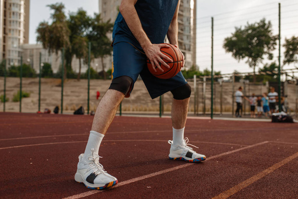 Jugador de baloncesto masculino sostiene una pelota en la cancha al aire libre. Atleta masculino en ropa deportiva en entrenamiento de streetball, estadio de verano
 - Foto, Imagen