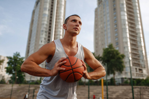 Kosárlabda játékos célja a dobás a szabadtéri pályán. Férfi sportoló sportruházatban tartja labda streetball edzés - Fotó, kép