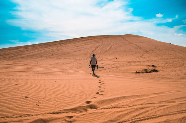 Wide shot of a person walking on a desert sand under a blue sky - Fotoğraf, Görsel
