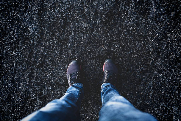 Overhead shot of a person wearing black shoes standing on black sand - Fotó, kép