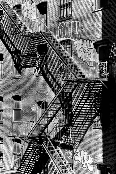 Vertical greyscale shot of metal staircases near an old building with windows - Фото, зображення